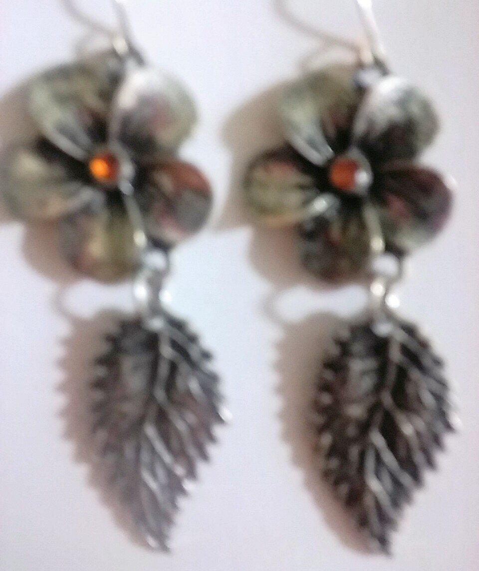 Antique style silver dangle earrings with a leaf charm attached to a flower.