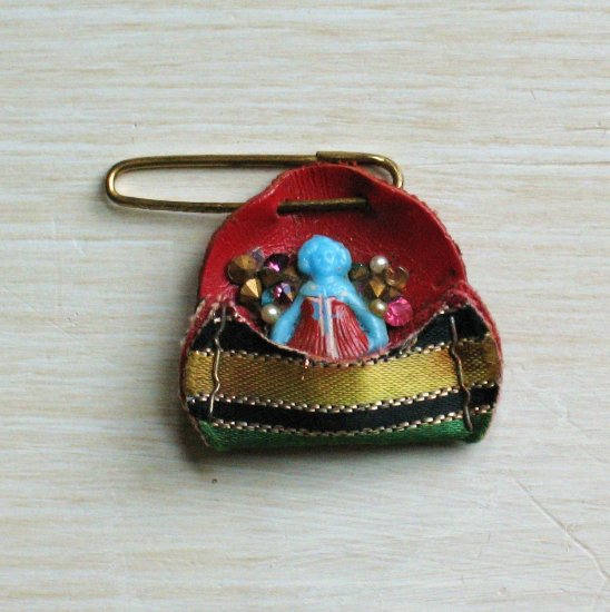 tiny blue celluloid doll pin with rhinestones in a leather pocket