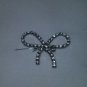 A broach or pin shaped like a bow, crystal and silver plated
