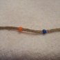 Blue, orange, green, and purple beads (4) on tan square
