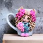 A hand made mug withdecor doll made of polymer clay.