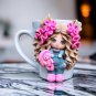 A hand made mug withdecor doll made of polymer clay.